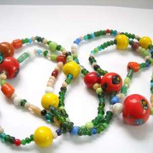 Op de afbeelding: Een meerstrengs ketting met groene, rode, gele en witte kralen. De ketting heeft grote, kleurrijke, ronde kralen met ingewikkelde patronen.
