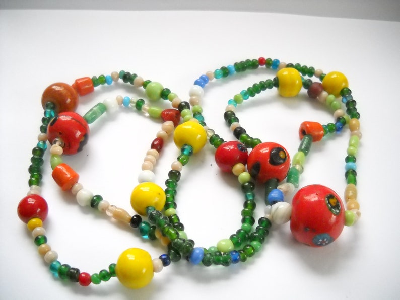 Op de afbeelding: Een meerstrengs ketting met groene, rode, gele en witte kralen. De ketting heeft grote, kleurrijke, ronde kralen met ingewikkelde patronen.