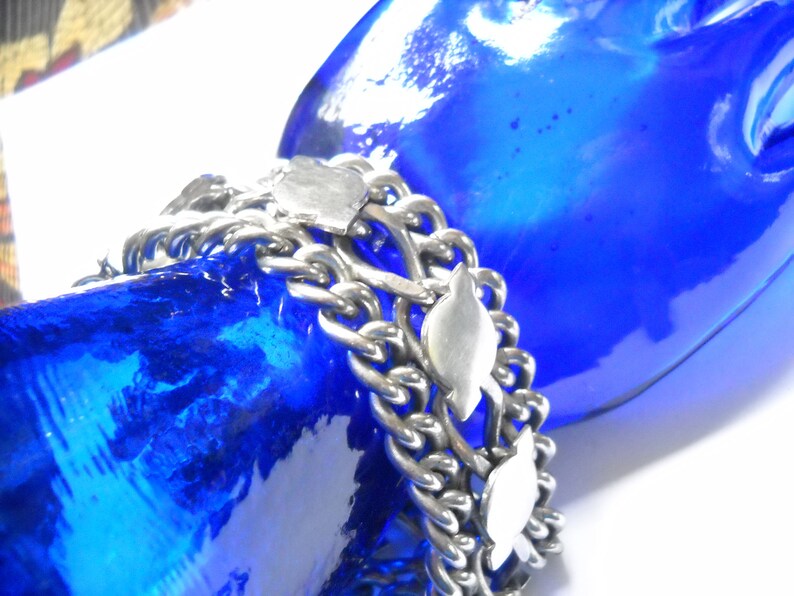 May include: A silver chain bracelet with multiple strands and decorative fish charms. The bracelet is on a blue mannequin hand.