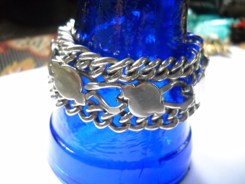 May include: A silver chain bracelet with a unique design featuring interlocking links and heart-shaped charms. The bracelet is displayed on a blue background.