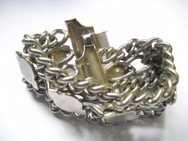 May include: A silver chain bracelet with a clasp and multiple decorative charms. The charms are shaped like hearts and have a smooth, polished finish.