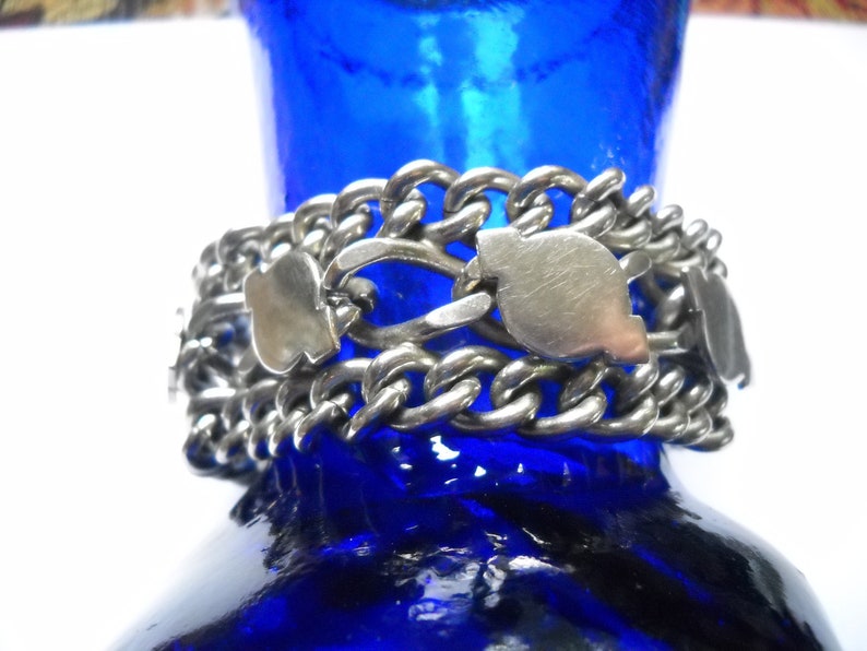May include: A silver chain bracelet with multiple links and silver charms in the shape of a heart. The bracelet is on a blue background.