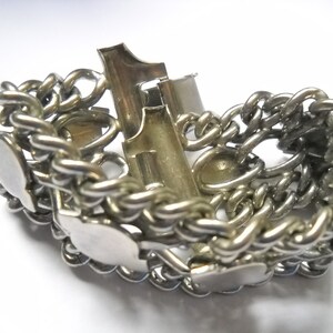 May include: A silver chain bracelet with a clasp and multiple decorative charms. The charms are shaped like hearts and have a smooth, polished finish.