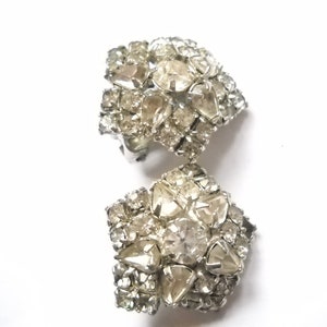 May include: A pair of silver tone clip-on earrings with a cluster of clear rhinestones in a flower shape.