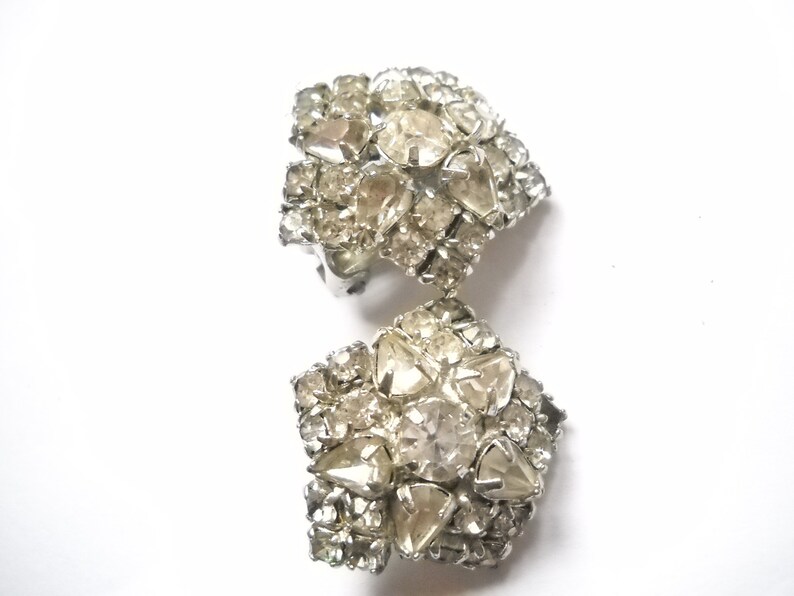 May include: A pair of silver tone clip-on earrings with a cluster of clear rhinestones in a flower shape.