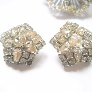 May include: A pair of silver tone earrings with a cluster of clear and iridescent rhinestones in a starburst design.