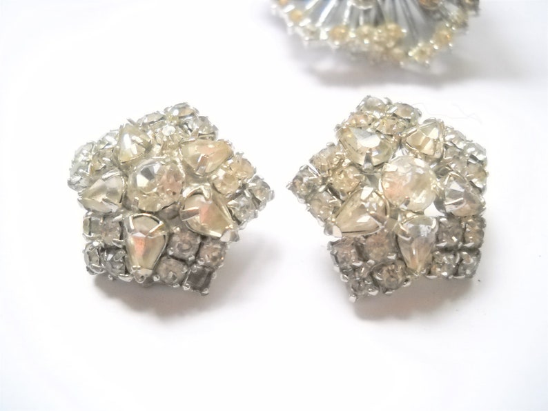 May include: A pair of silver tone earrings with a cluster of clear and iridescent rhinestones in a starburst design.