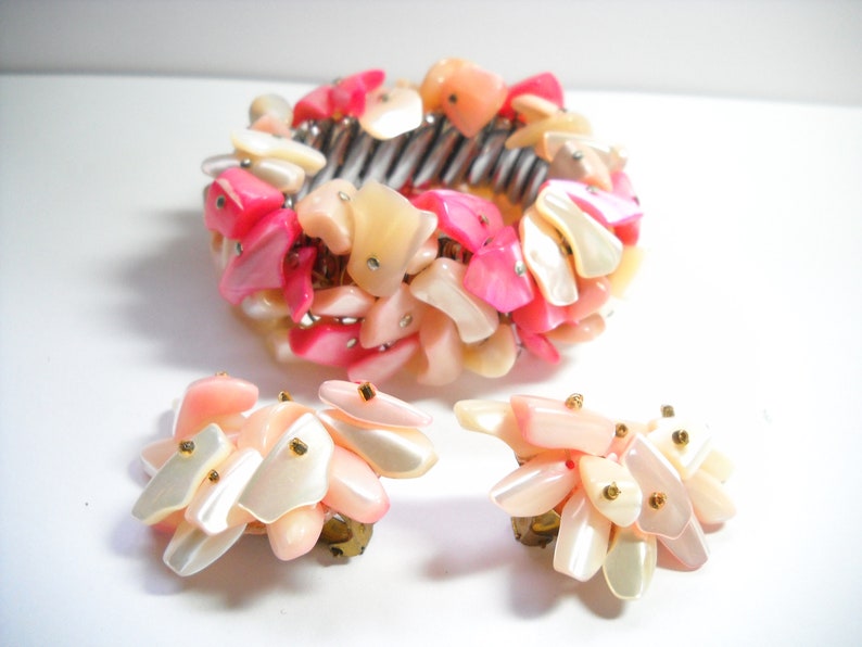 K&ouml;nnte beinhalten: Ein Set aus rosa und wei&szlig;en Muschel-Schmuck, bestehend aus einem Armband und einem Paar Ohrringen. Das Armband besteht aus vielen kleinen, unregelm&auml;&szlig;ig geformten Muscheln, und die Ohrringe sind im Design &auml;hnlich.