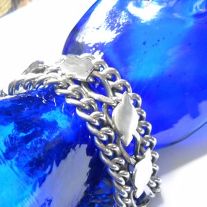 May include: A silver chain bracelet with multiple strands and decorative fish charms. The bracelet is on a blue mannequin hand.