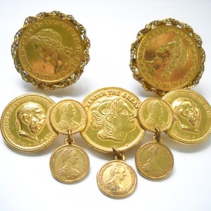 May include: Gold-tone coin earrings with a dangling chain of smaller coins. The larger coins feature the profile of a person, while the smaller coins feature a profile of a woman. The larger coins have text around the edge.