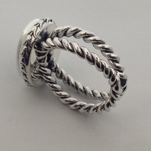 May include: Silver ring with a twisted rope design. The ring is made of two bands of twisted metal that are intertwined.