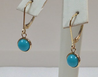 Puede incluir: Un par de pendientes de oro con piedras turquesa. Los pendientes son de estilo colgante con un diseño sencillo.