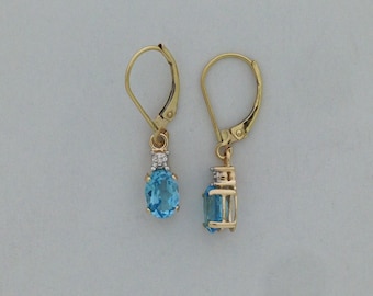 Könnte beinhalten: Ein Paar Ohrringe mit Brisurverschluss aus Gold, besetzt mit oval geschliffenen blauen Topas-Edelsteinen, die unter kleinen, runden, klaren Akzentsteinen hängen. Die Ohrringe sind in einer Goldfassung gearbeitet.