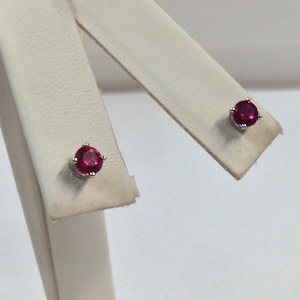May include: A pair of ruby stud earrings set in silver. The earrings are small and round, with a bright red color.