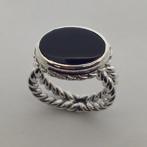 May include: A silver ring with a black oval gemstone set in a bezel setting. The band is a twisted rope design.
