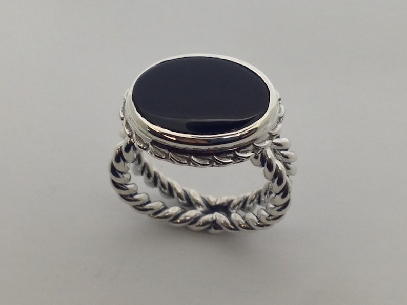 May include: A silver ring with a black oval gemstone set in a bezel setting. The band is a twisted rope design.