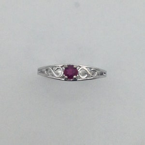 May include: A silver ring with a delicate, openwork design featuring a single, round, red ruby gemstone.