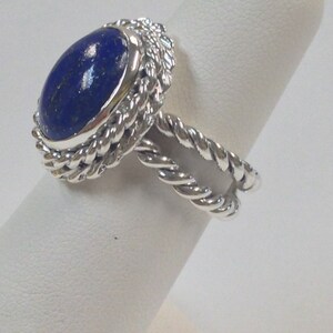 Puede incluir: Un anillo de plata con una piedra ovalada de lapisl&aacute;zuli azul engastada en una banda de dise&ntilde;o de cuerda trenzada.