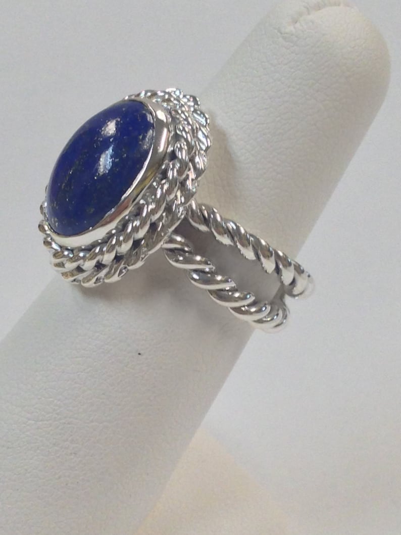 Puede incluir: Un anillo de plata con una piedra ovalada de lapisl&aacute;zuli azul engastada en una banda de dise&ntilde;o de cuerda trenzada.
