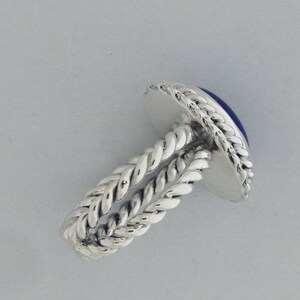 Puede incluir: Un anillo de plata con una piedra preciosa azul engastada en una banda retorcida.