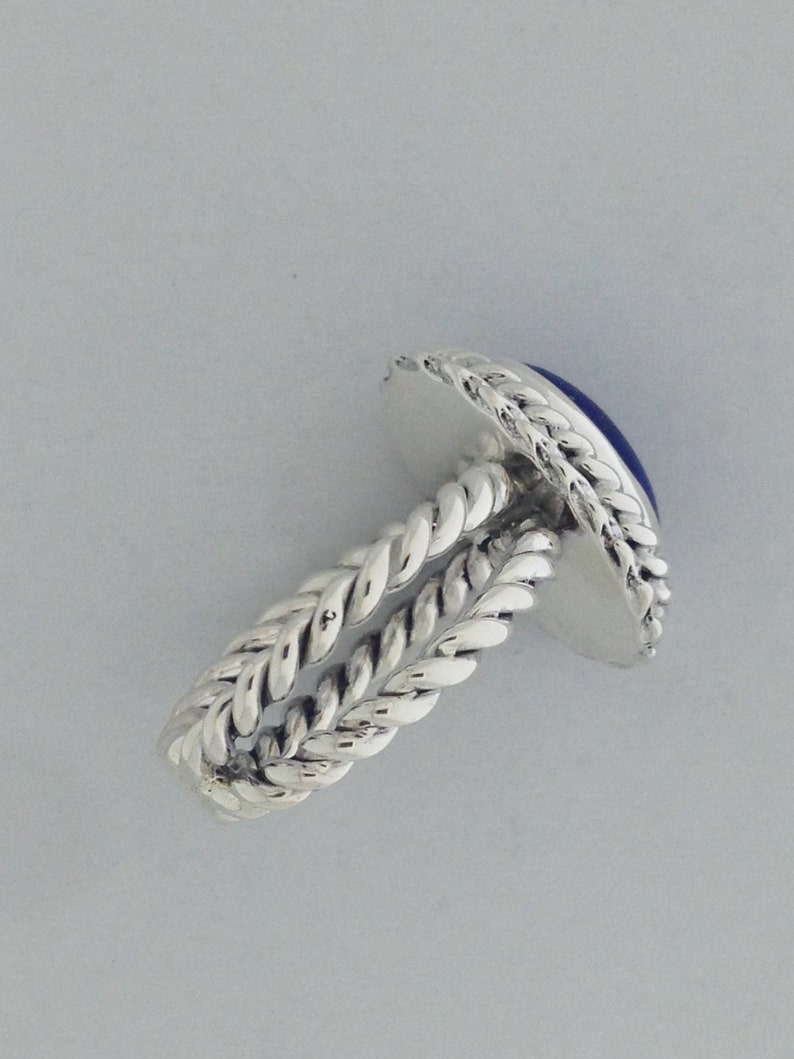 Puede incluir: Un anillo de plata con una piedra preciosa azul engastada en una banda retorcida.