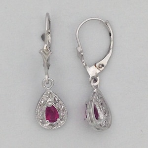 May include: A pair of silver-toned drop earrings. Each earring features a pear-shaped, deep red gemstone surrounded by a decorative, openwork frame. The earrings have a lever-back closure.