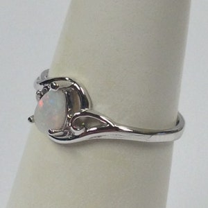 May include: A silver-toned ring featuring a pear-shaped, iridescent opal gemstone. The ring has a delicate, swirling design around the stone and along the band, showcasing a classic and elegant style. The opal displays a play of colors.