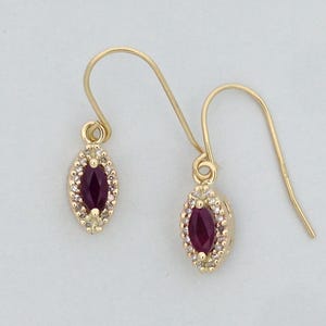 May include: A pair of gold earrings featuring a marquise-shaped ruby gemstone set in a halo of smaller white gemstones.