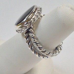 May include: A silver ring with a black oval gemstone set in a detailed floral design. The band is a twisted rope design.
