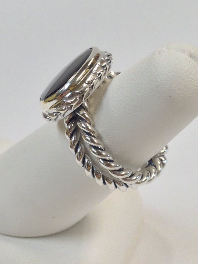 May include: A silver ring with a black oval gemstone set in a detailed floral design. The band is a twisted rope design.