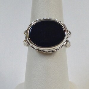 May include: A silver ring with a black oval gemstone set in a decorative bezel. The ring has a rope-like design around the bezel.