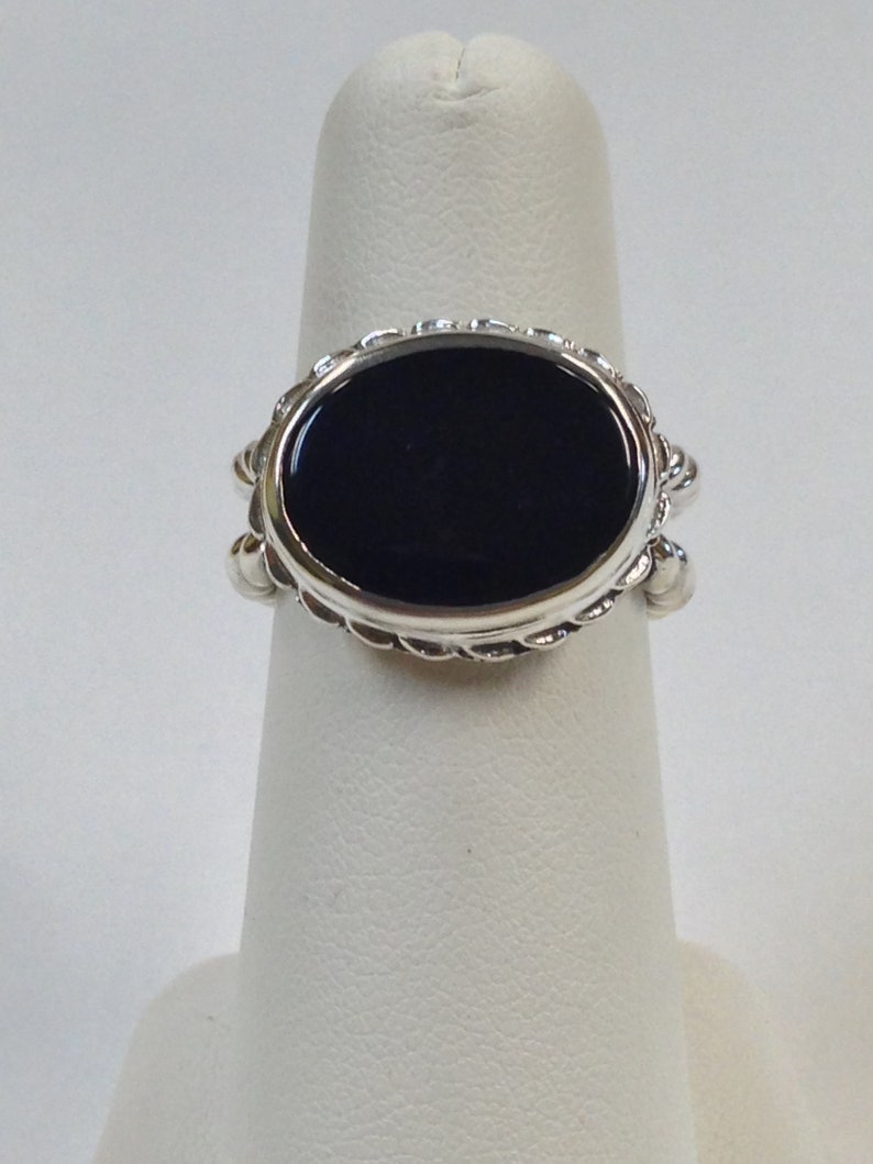 May include: A silver ring with a black oval gemstone set in a decorative bezel. The ring has a rope-like design around the bezel.