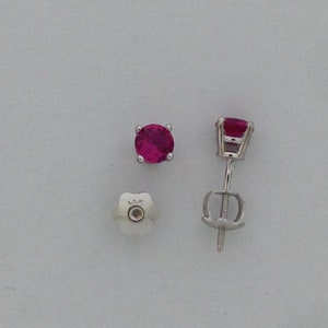 May include: A pair of ruby stud earrings with a silver setting. The earrings are shown from the top and the back.