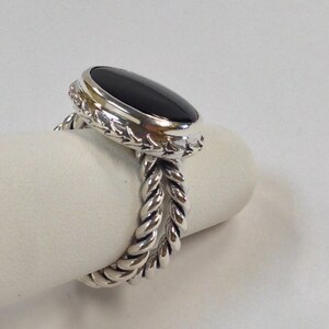 May include: A silver ring with a black oval gemstone set in a twisted rope band.