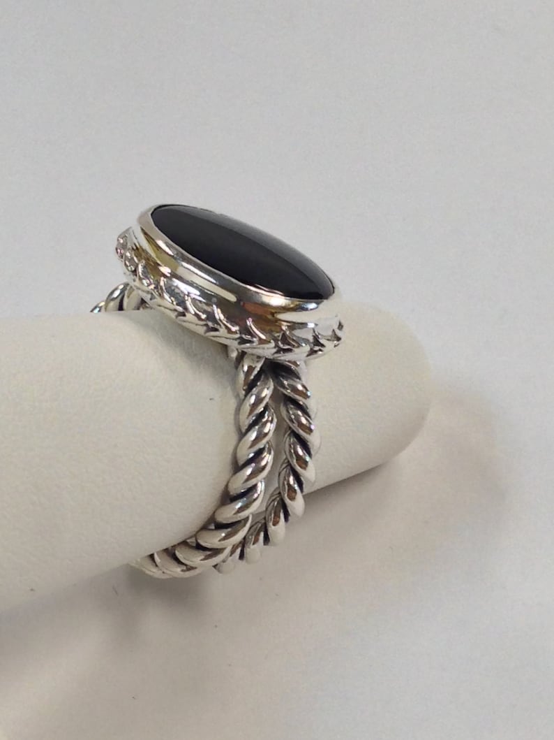 May include: A silver ring with a black oval gemstone set in a twisted rope band.