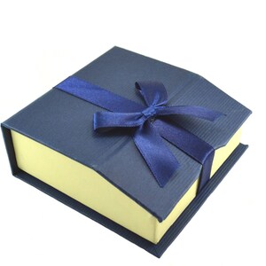Puede incluir: Una caja de regalo azul con interior amarillo y una cinta de raso azul atada en un lazo.