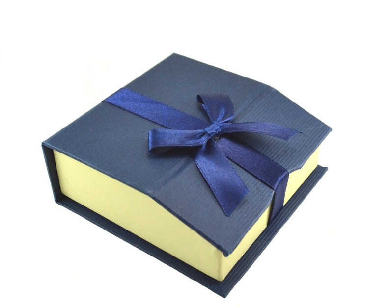Puede incluir: Una caja de regalo azul con interior amarillo y una cinta de raso azul atada en un lazo.