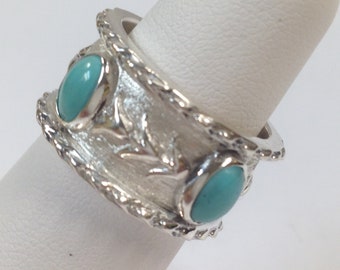 Puede incluir: Un anillo de plata con dos piedras turquesa engastadas en la banda. La banda es texturizada y tiene un diseño de una rama con hojas.