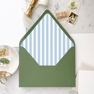 May include: An open green envelope with a blue and white striped interior. The envelope is surrounded by stationery, including stamps, a gold wax seal, and blank white cards. The stamps feature images of a butterfly, a tree, and historical figures.