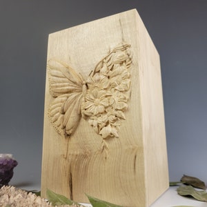 May include: A wooden box with a carved butterfly and flowers design. The box is made of light wood and has a natural finish.