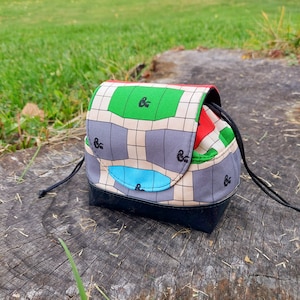 Peut inclure: Un petit sac à cordon noir et blanc avec un motif vert, rouge et bleu. Le sac a un cordon noir et une bordure noire autour du haut.