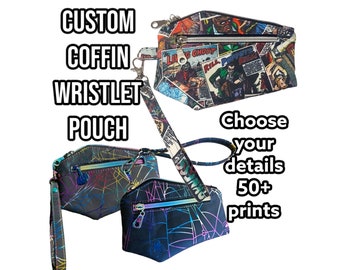 May include: Three coffin-shaped wristlet pouches with wrist straps. One features a vintage comic book print, while two feature a black fabric with a colorful spiderweb pattern. Text reads: CUSTOM COFFIN WRISTLET POUCH and Choose your details 50+ prints.
