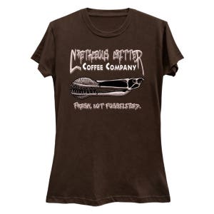 Puede incluir: Camiseta marr&oacute;n con un gr&aacute;fico blanco de un logotipo de una empresa de caf&eacute;. El logotipo dice "Meticulous Critter Coffee Company" y presenta una imagen estilizada de un pez prehist&oacute;rico. El texto debajo del logotipo dice "Fresco, no fosilizado."
