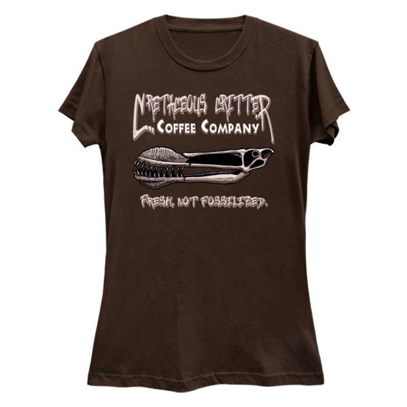 Puede incluir: Camiseta marr&oacute;n con un gr&aacute;fico blanco de un logotipo de una empresa de caf&eacute;. El logotipo dice "Meticulous Critter Coffee Company" y presenta una imagen estilizada de un pez prehist&oacute;rico. El texto debajo del logotipo dice "Fresco, no fosilizado."