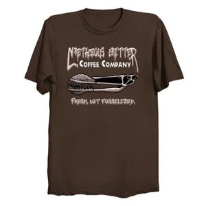 Puede incluir: Camiseta marr&oacute;n con un gr&aacute;fico blanco de una cuchara de caf&eacute; y el texto "N'righteous Brews Coffee Company" y "Fresh, not fossilized."