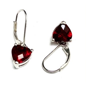 Pode incluir: Um par de brincos de prata em forma de coração com detalhes de pedras preciosas vermelhas. Os brincos têm fecho de pressão.