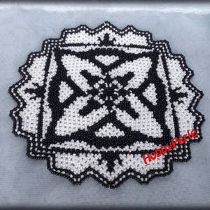 May include: Black and white beaded round doily with a geometric pattern. The doily has a scalloped edge.