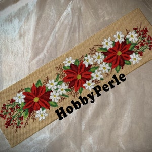 May include: A beige canvas with a red and white floral design embroidered on it. The design features poinsettia flowers, white flowers, and green leaves. The text "HobbyPerle" is printed in black on the canvas.