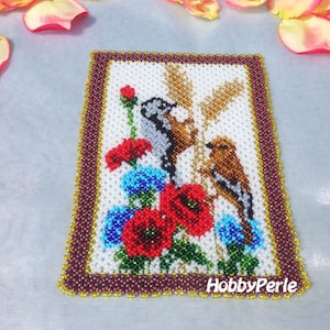 Pode incluir: Uma imagem de contas de dois pássaros empoleirados em um galho com flores vermelhas e azuis. A imagem é emoldurada com contas marrons e douradas e tem o texto "HobbyPerle" na parte inferior.