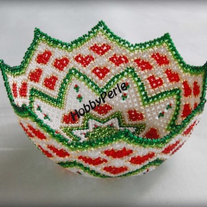 Puede incluir: Un cuenco de cuentas blancas con un patrón geométrico en rojo y verde. El cuenco tiene forma de estrella y un borde festoneado. El texto "HobbyPerle" es visible en el cuenco.
